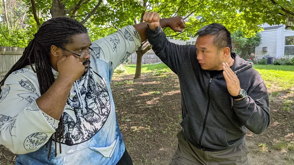 Sam lunges forward with his High Block, driving up and under Kysean’s strike. – Blocking a Punch Part 2