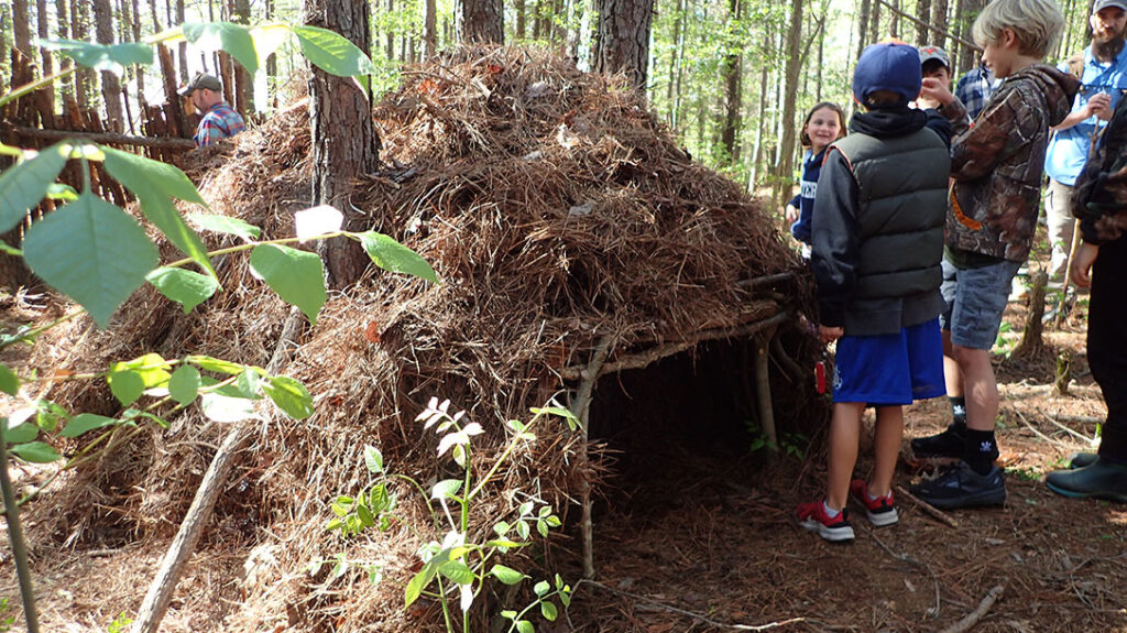 A debris hut is taught during the class as a group build. Individuals then get their pictures taken inside. This shelter takes about 2-hours to complete alone, but in a group, it took only 20 minutes.