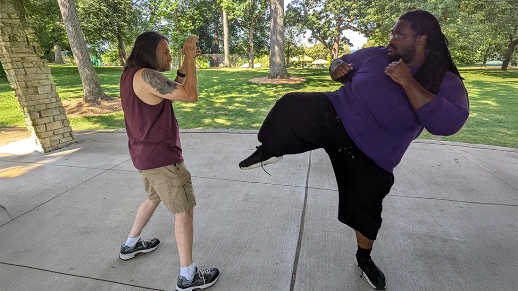 Don, who is outside of his striking range, prepares for an attack from Kysean, who is much larger than he is. Kysean is throwing a roundhouse kick from an outside range.