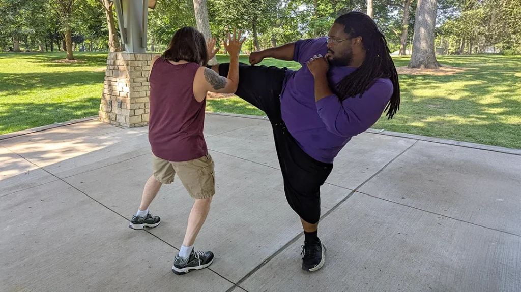 He takes a 45-degree sidestep and uses a double forearm block to stop Kysean’s roundhouse kick.